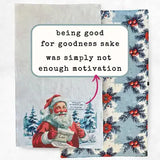 A Christmas-themed tea towel shown folded to display both sides. The front side features an illustration of Santa Claus holding a letter in a snowy landscape, with a white text bubble overlay that reads 'being good for goodness sake was simply not enough motivation' and a pink arrow pointing to it.