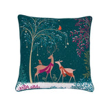 A square decorative throw pillow featuring a festive winter woodland design. The dark teal background is decorated with two deer in pink and orange sweaters, a tree with hanging stars, birds, and snowy ground.