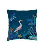 A square teal throw pillow featuring a detailed embroidered design of a heron surrounded by tropical foliage in shades of blue, green, orange, and white, set against a plain white background.