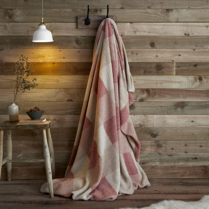 Pink and beige checkered blanket draped over a wooden chair against a wooden wall.
