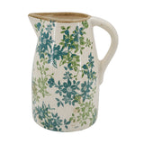 A ceramic pitcher with a cream-colored body, decorated with a blue and green floral pattern, and featuring a natural unglazed brown rim.