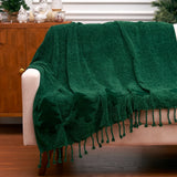 Green blanket with tassels draped over a beige armchair in a room with wooden furniture and decorative items.