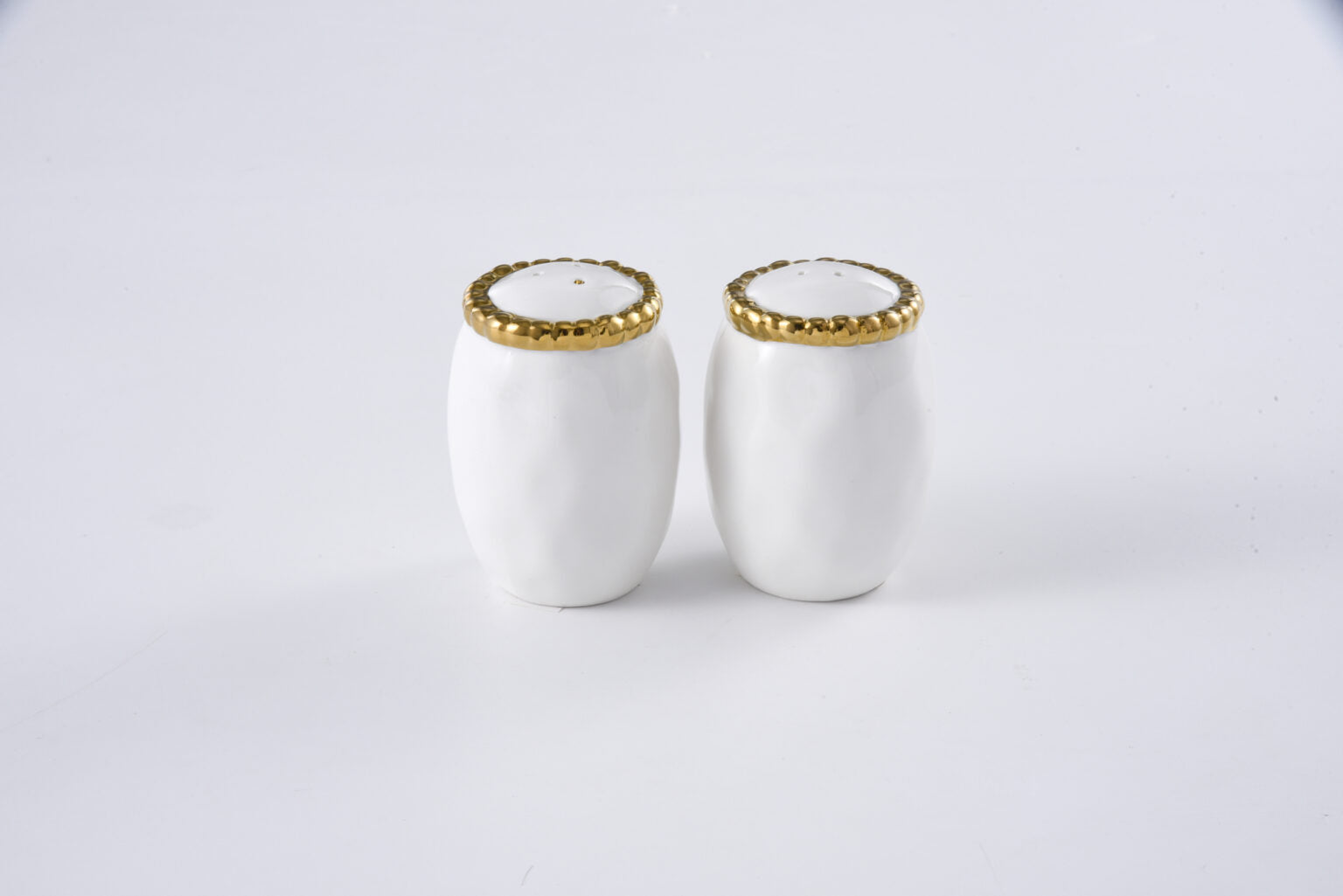 Two white ceramic salt and pepper shakers with gold rims on a light gray background