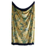 A draped yellow silk scarf with a green botanical and bird pattern, finished with a dark navy blue fringed border at the top and bottom.