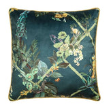 A square decorative throw pillow featuring a dark teal velvet fabric with an intricate botanical print of green leaves, yellow and white flowers, and small birds, finished with a gold piped edge.