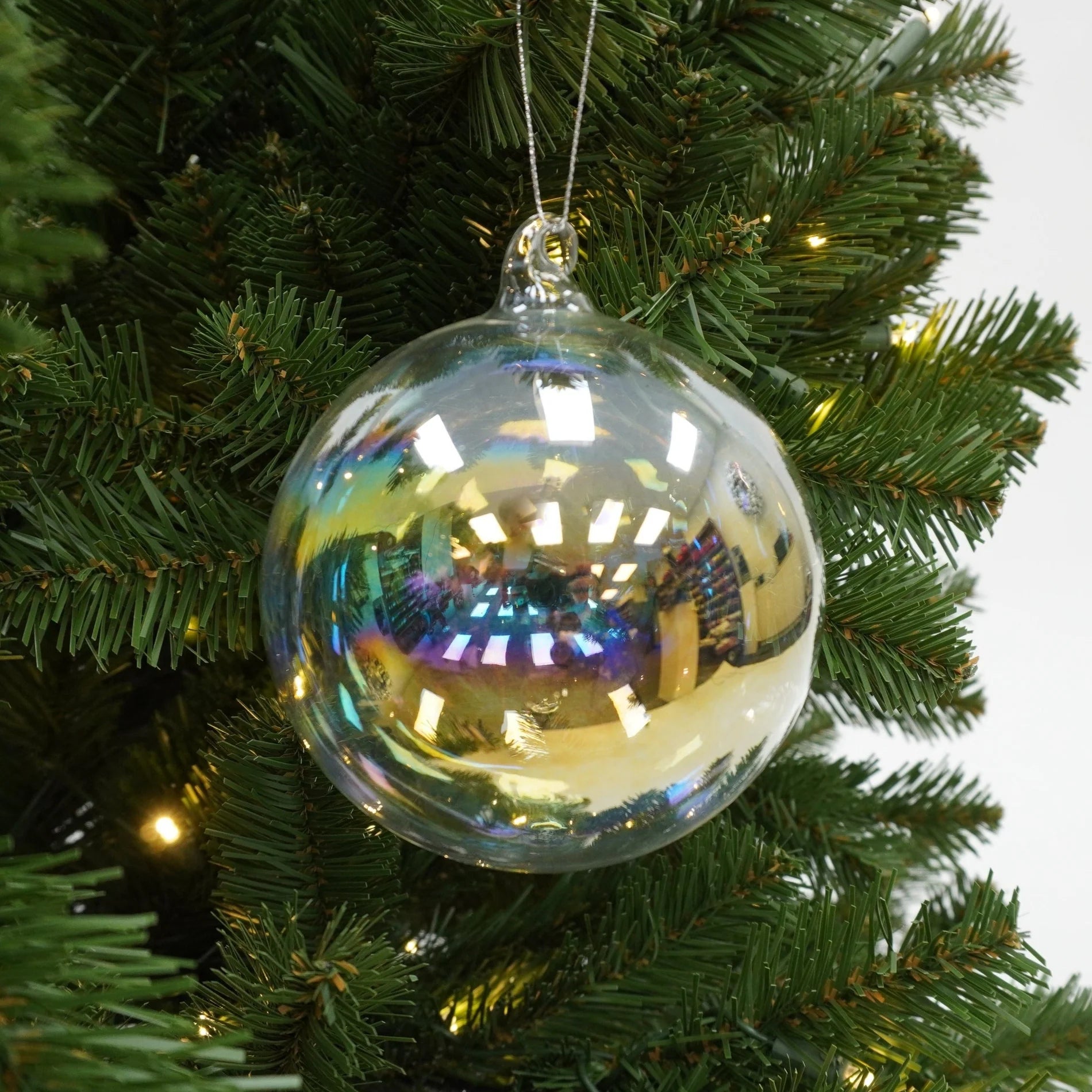Clear glass ornament on a Christmas tree with green branches and lights.