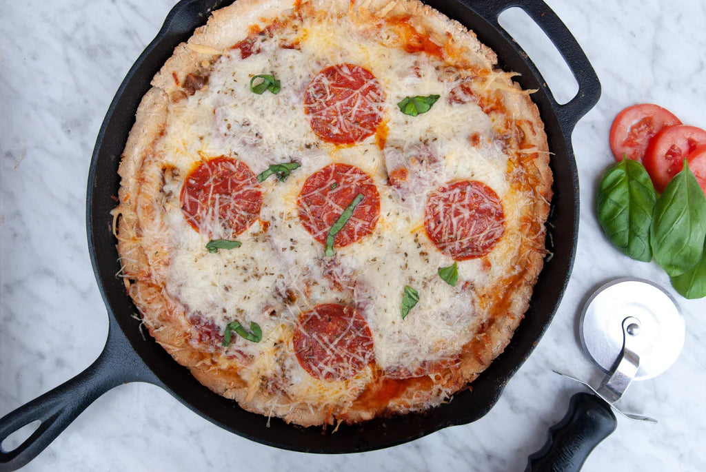 Personal-sized pizza with pepperoni and cheese in a black pan on a marble surface.