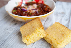 Cornbread slices with a bowl of chili on a wooden surface