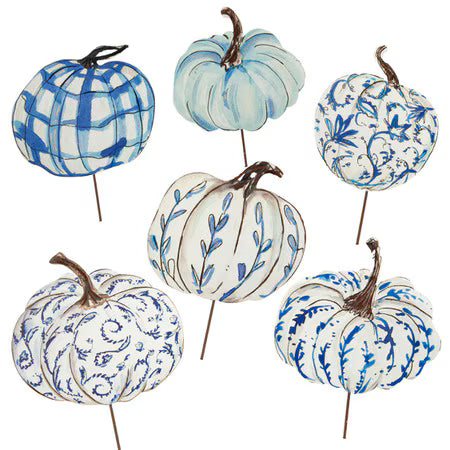 Six decorative faux pumpkins on thin metal stakes, arranged on a white background. The pumpkins have white and blue painted patterns including plaid, floral, and leaf motifs, with brown stems.