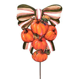 A decorative autumn garden stake featuring a cluster of orange pumpkins tied with a striped bow in red, white, and dark green, mounted on a thin black stake against a plain white background.