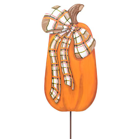 An orange decorative pumpkin sign with a brown stem and a large plaid bow in white, orange, green, and brown, mounted on a thin stake against a plain white background.