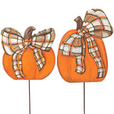 Two orange pumpkin yard signs with brown stems and large plaid bows in beige, white, orange, and green, mounted on thin stakes against a white background.