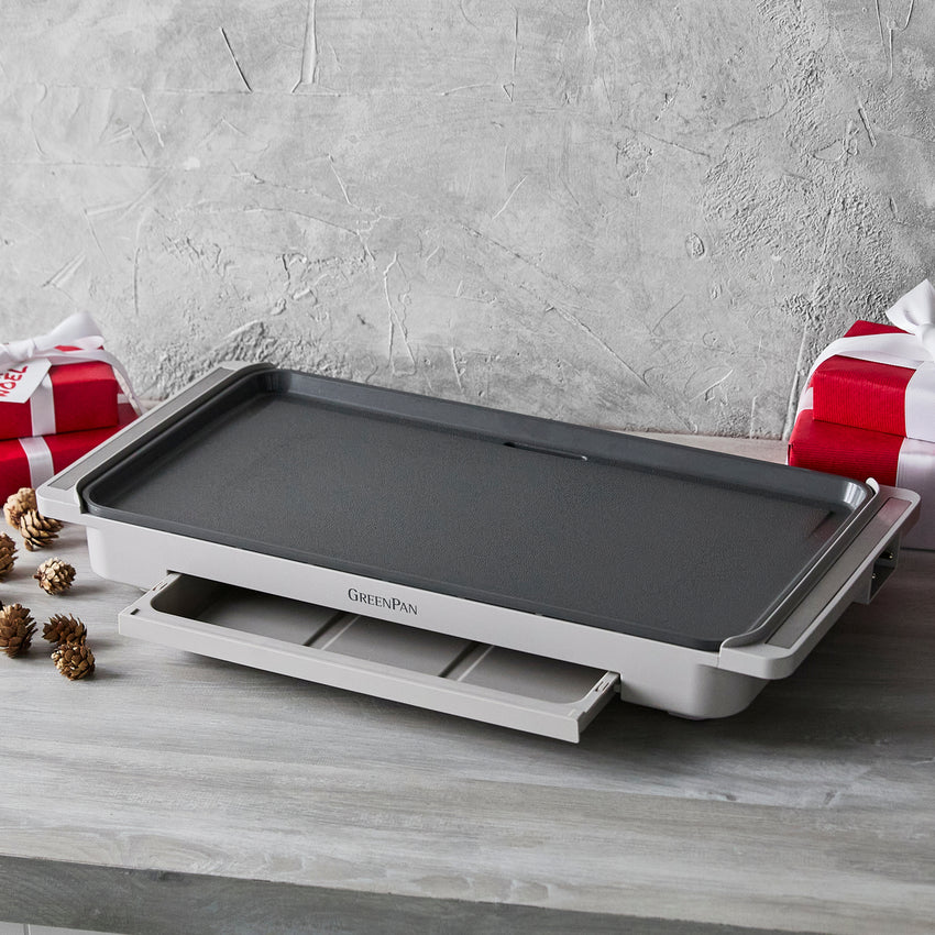 Gray electric griddle on a wooden surface with a gray textured wall in the background