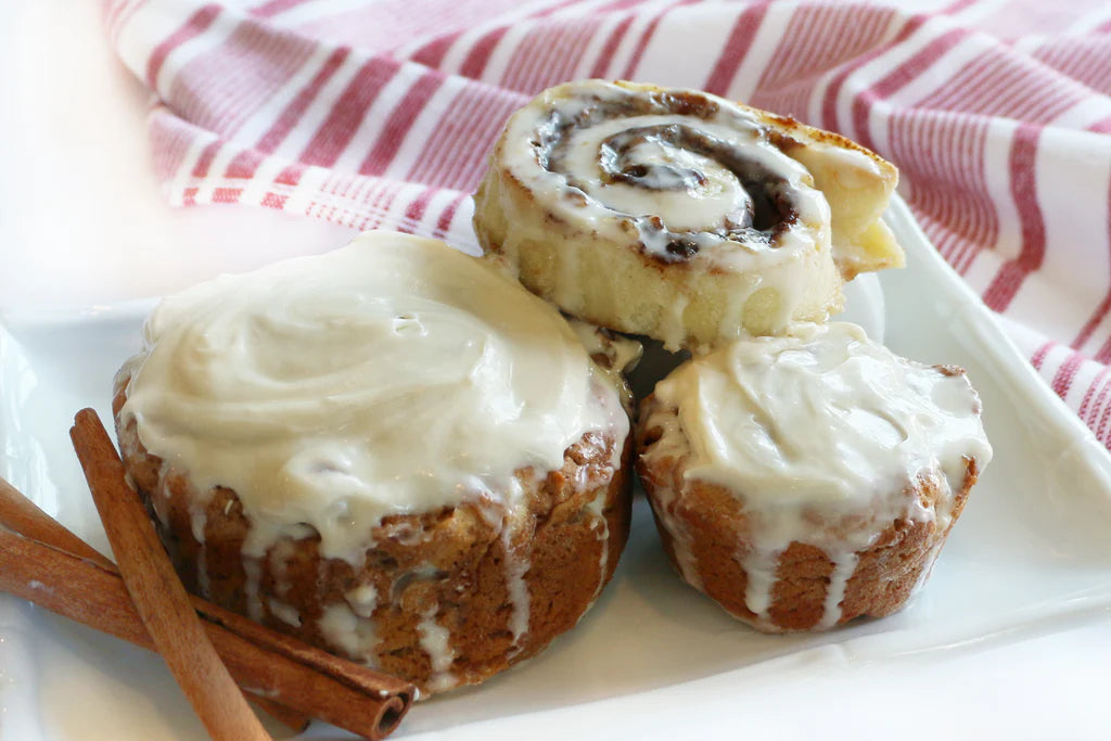 Three cinnamon rolls with cream cheese frosting on a white plate with a red and white striped towel in the background.
