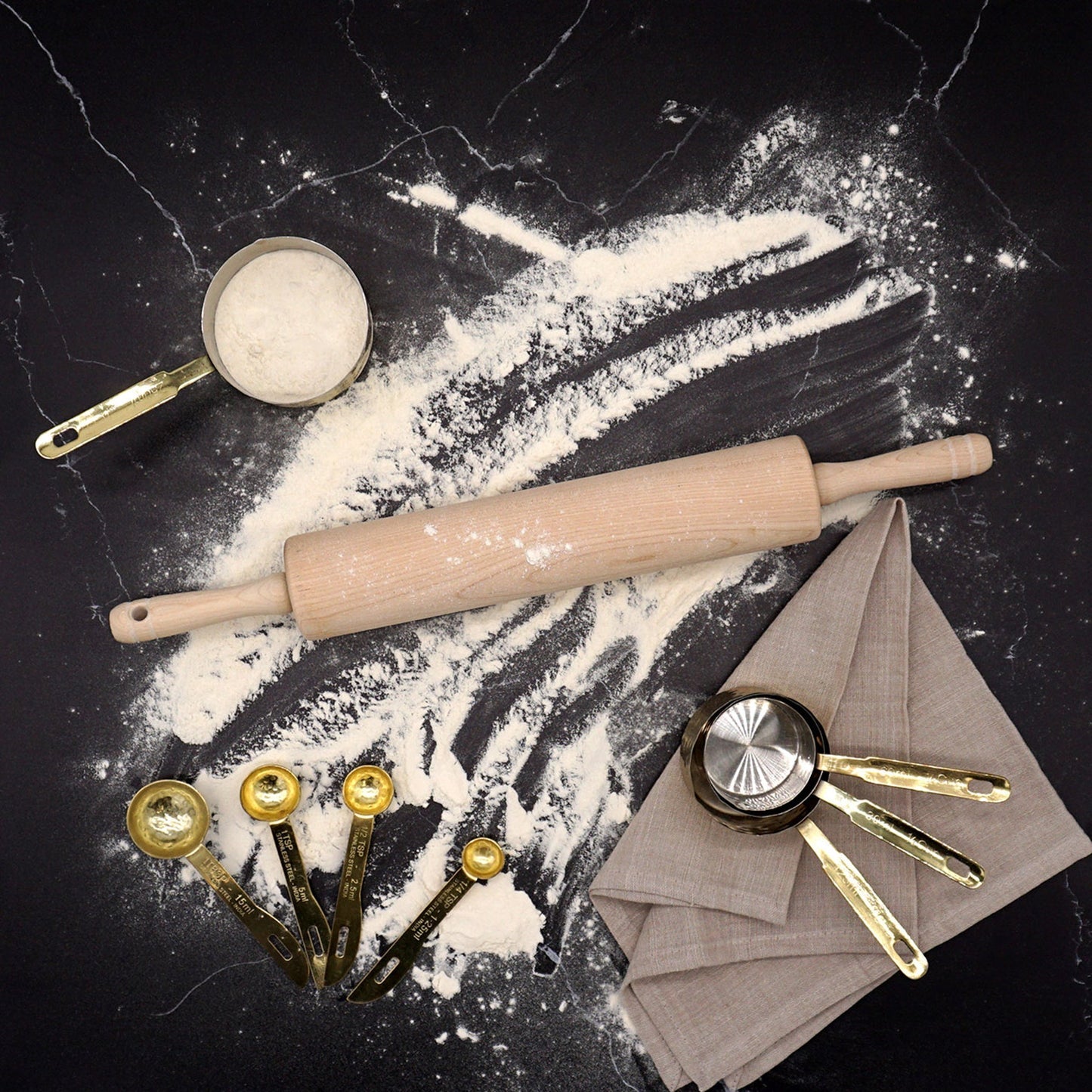 Baking tools including a rolling pin, measuring cups, and flour on a dark surface.