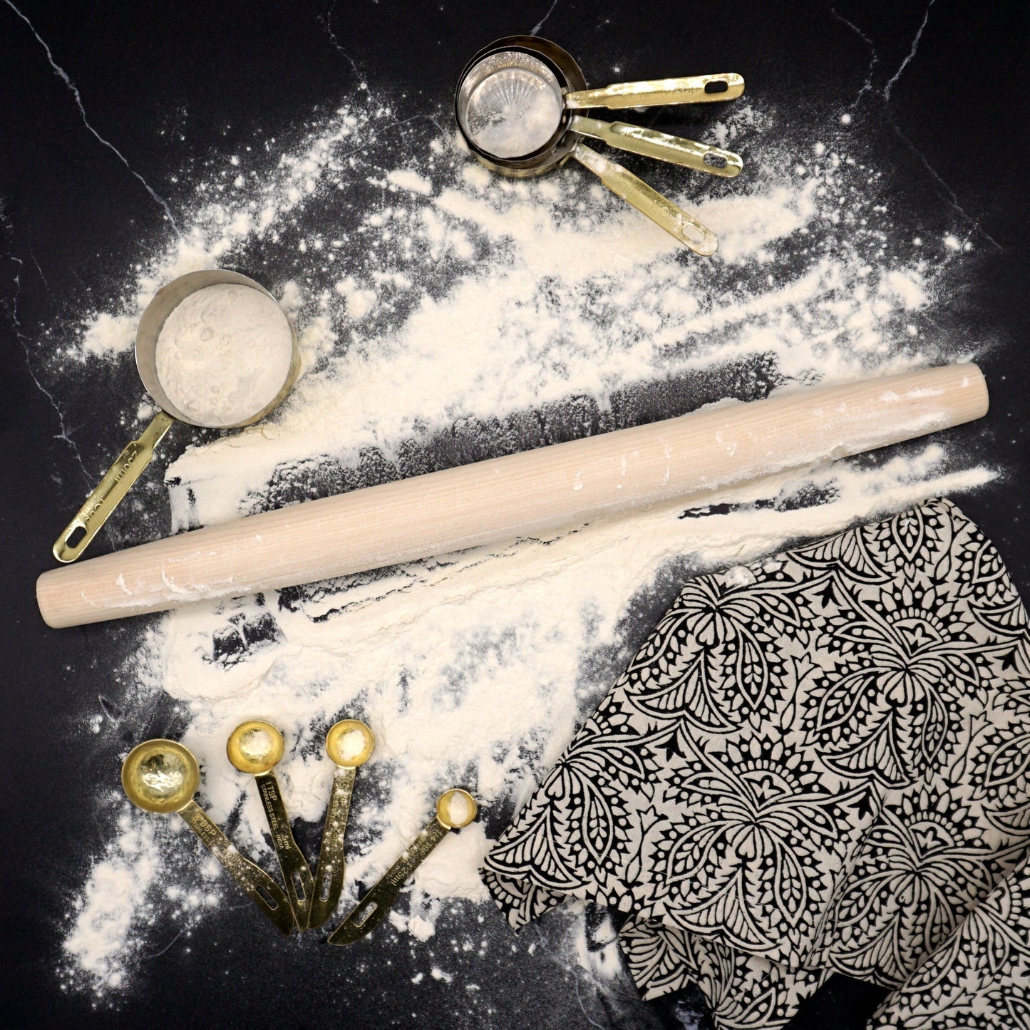 Rolling pin and measuring cups on a black surface with flour