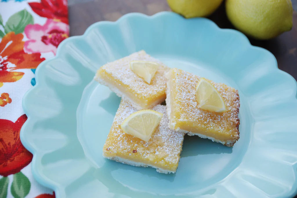 Two lemon bars on a blue plate with lemons in the background
