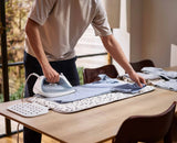 Person ironing clothes on a wooden table with ironing pad a window in the background