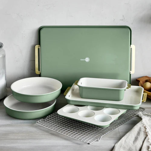 Set of green ceramic cookware including bowls, baking tray, and muffin tin on a wooden surface.