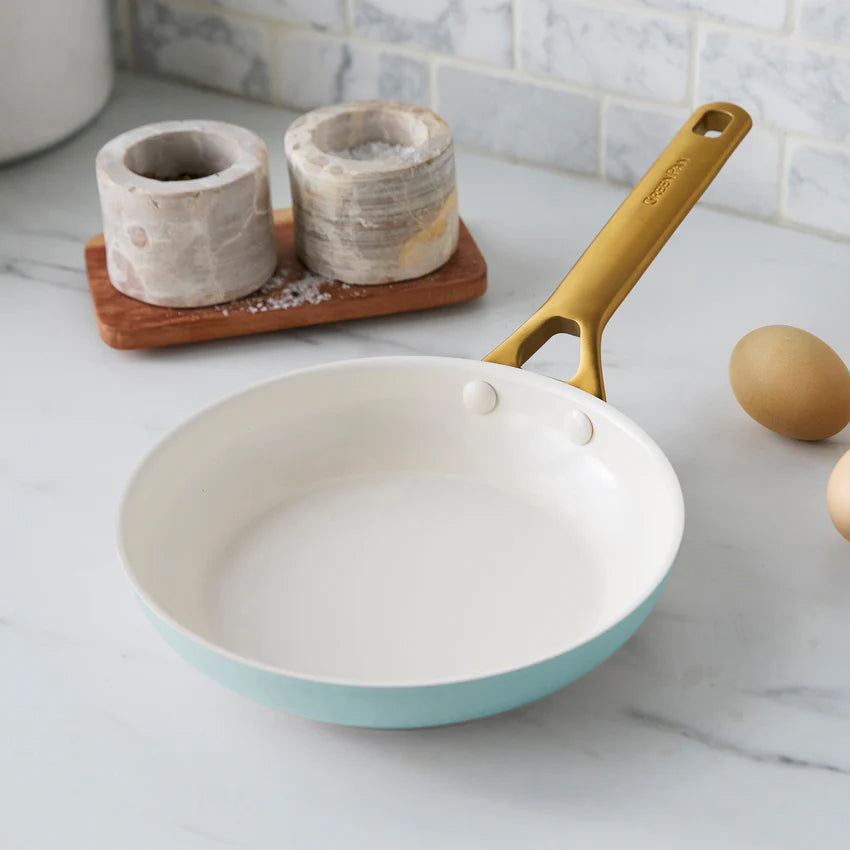 White frying pan with gold handle on a marble countertop