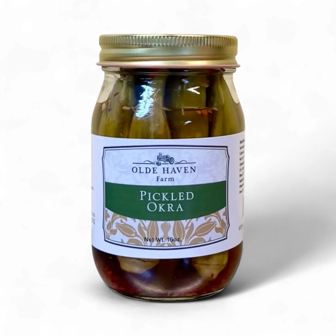 A glass jar of Olde Haven Farm Pickled Okra with a white and green label and a gold metal lid, set against a plain white background.