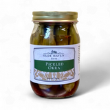 A glass jar of Olde Haven Farm Pickled Okra with a white and green label and a gold metal lid, set against a plain white background.