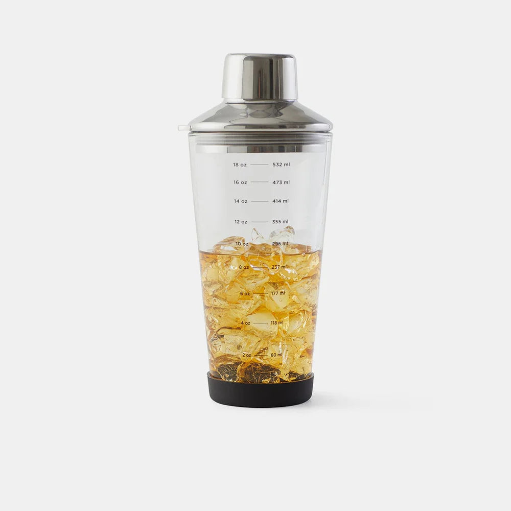 Clear cocktail shaker with metal top and black base filled with ice and liquid on a white background