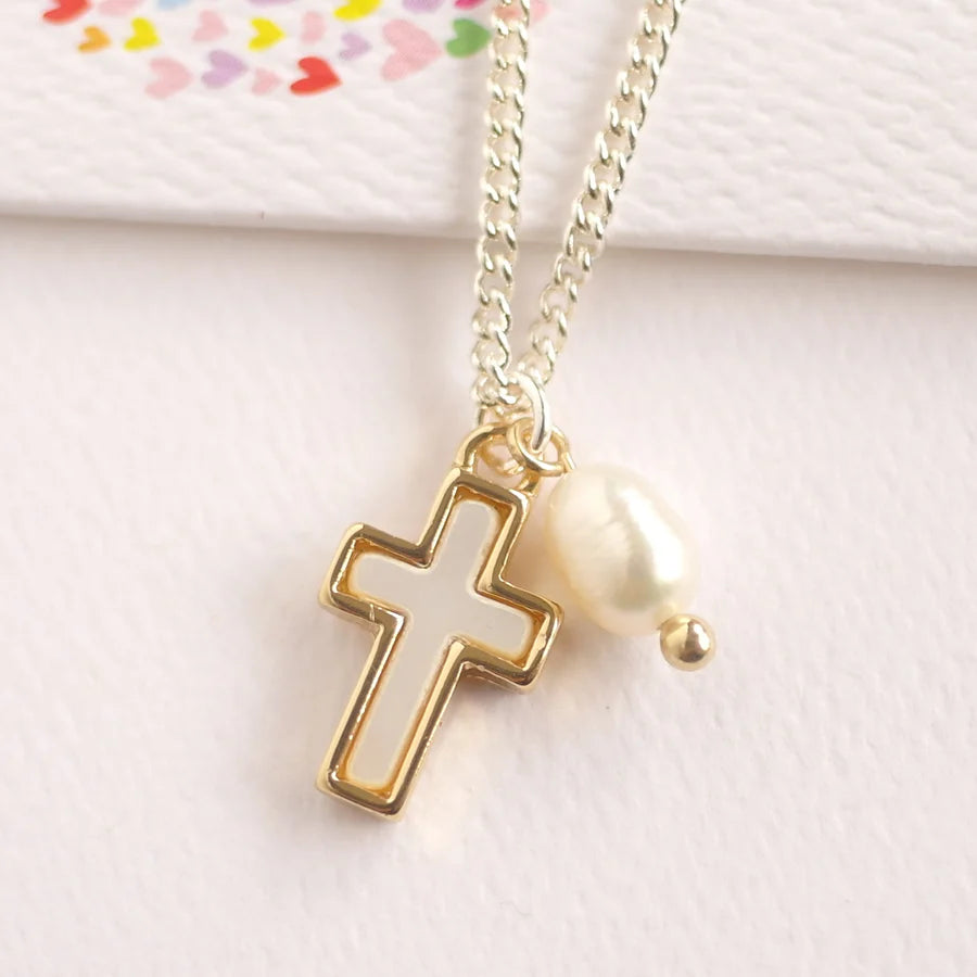 Gold cross necklace with a pearl pendant on a light pink background