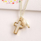 Gold cross necklace with a pearl pendant on a light pink background