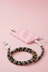 A pink phone case with a white charging cable attached, styled with a beaded phone strap made of black and leopard-print beads on a solid pink background.