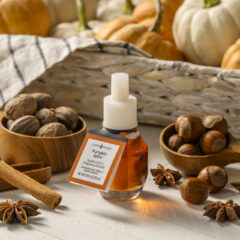 A small glass bottle of Cinnamon Creek Fragrances Pumpkin Spice refill with a white dropper cap, surrounded by autumn spices and pumpkins on a rustic tabletop.