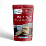 A stand-up pouch of Mon's Place Cinnamon Snickerdoodles on a clean white background. The packaging is primarily dark red with white text and a photo of the cookies on the front.