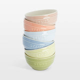 Set of four colorful Staub bowls stacked on a white background