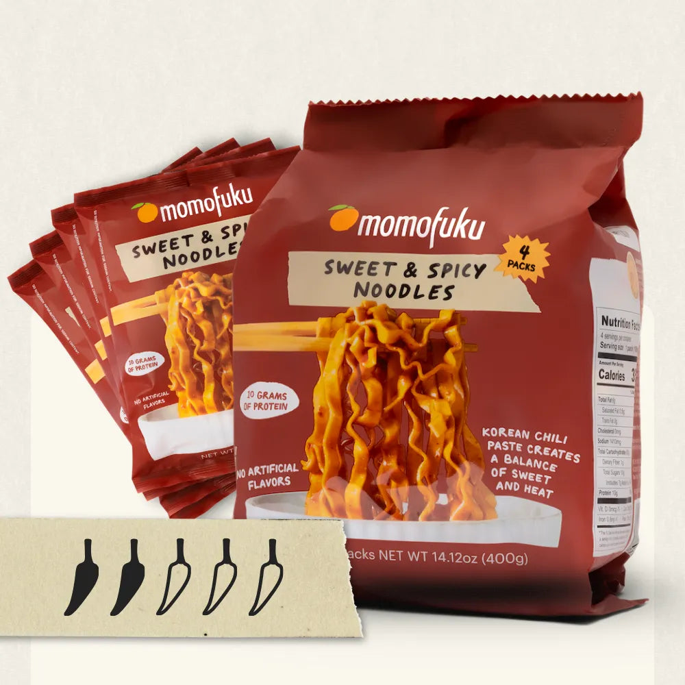 Momofuku Sweet & Spicy Noodles in a large red bag with several smaller single-serve packets fanned behind it. A small card at the bottom shows five pepper illustrations.