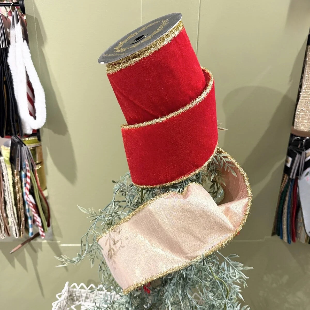 Red ribbon spool on a decorative stand with greenery against a neutral background
