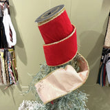 Red ribbon spool on a decorative stand with greenery against a neutral background