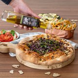 Person pouring olive oil over a pizza with salad and fries on a wooden table