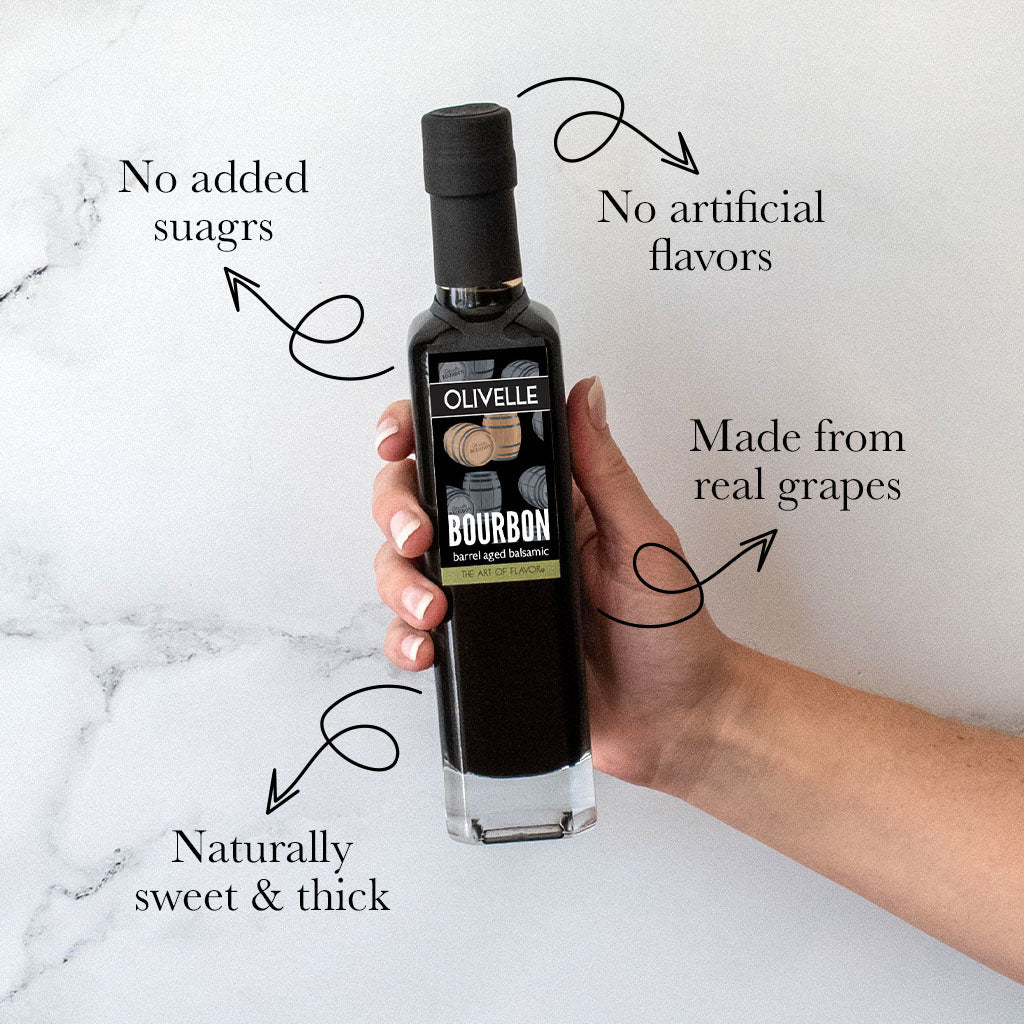 Hand holding a bottle of Olivelle bourbon barrel-aged balsamic on a marble surface with text highlighting its features.