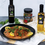 Plated dish with lemon slices and herbs, accompanied by Olivelle oil and seasoning bottles on a white background.