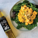 Plate of scrambled eggs with greens and a bottle of Olivelle Black Truffle olive oil on a light background