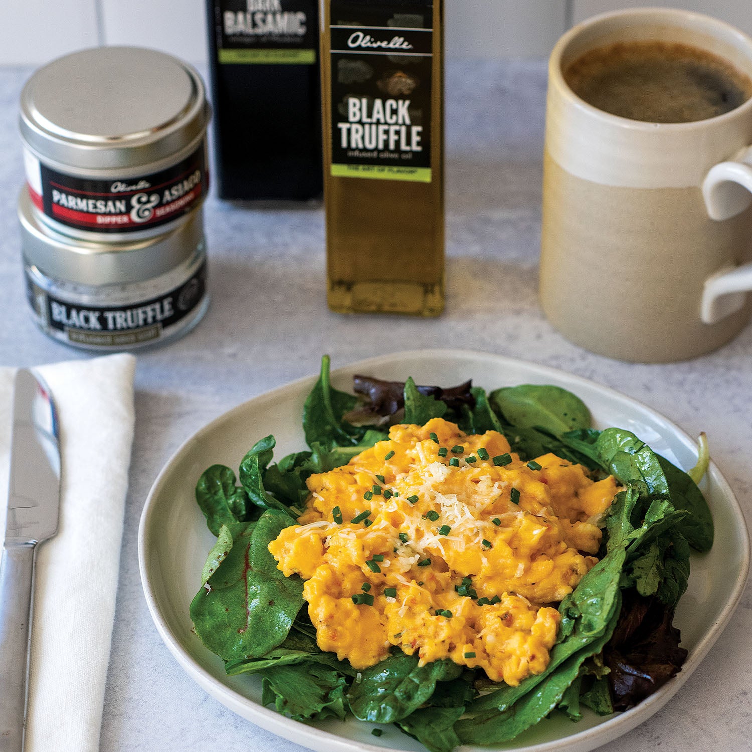 Plate of scrambled eggs on greens with a cup of coffee and Parmesan cheese in the background.