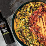 Pizza with various toppings in a Staub pan next to a bottle of Olivelle olive oil.