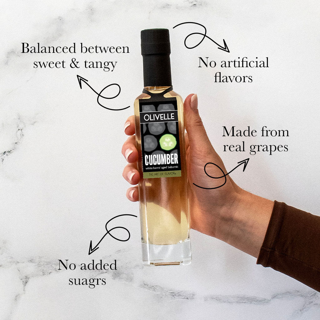 Hand holding a bottle of Olivelle cucumber product on a marble surface with text highlighting features.