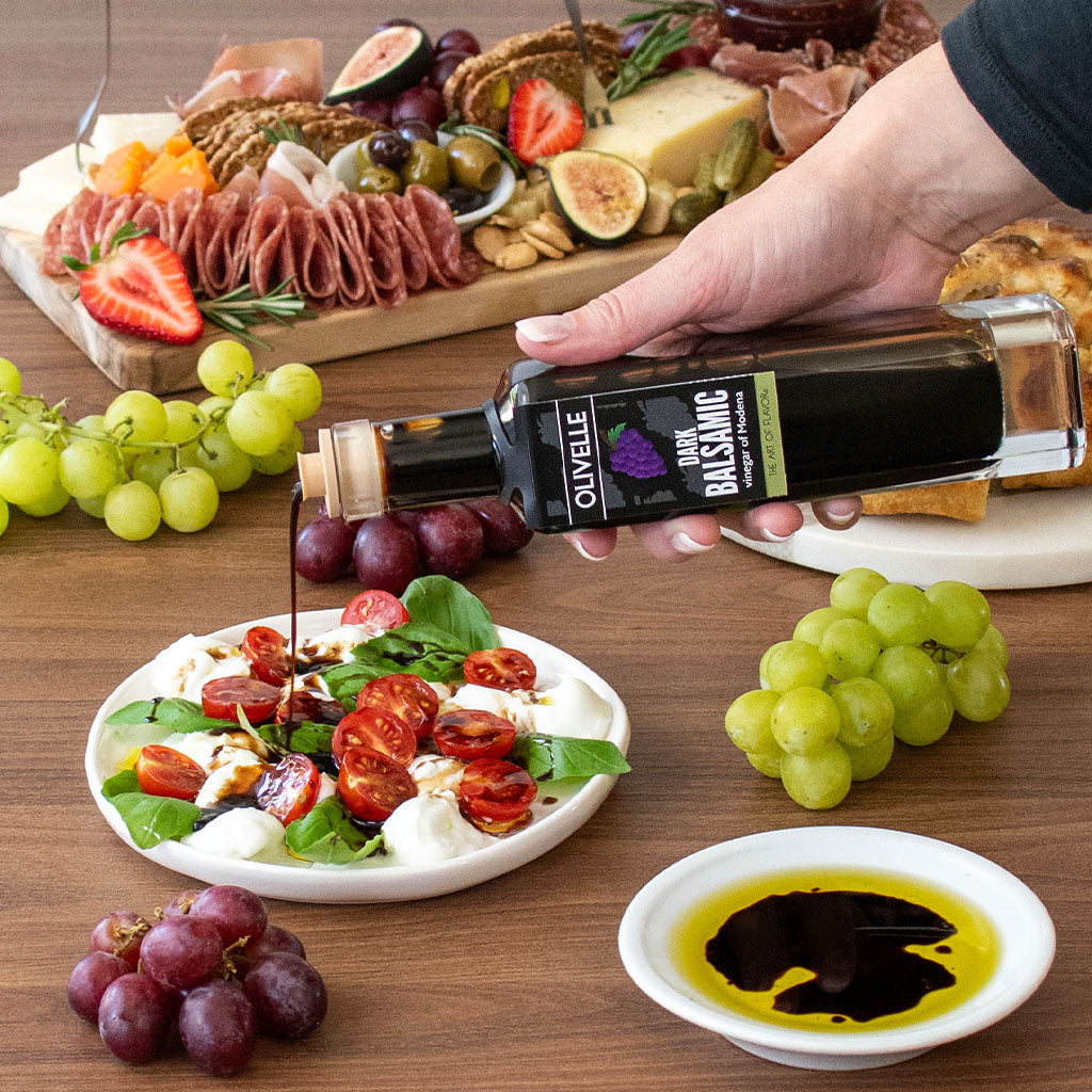 Person pouring olive oil over a salad with a charcuterie board in the background