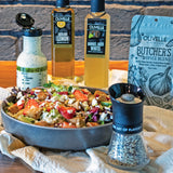 Assorted Olivelle products including a salad, olive oil bottles, and a spice blend on a wooden surface.