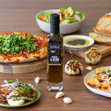 Olivelle Garlic & Herb infused olive oil bottle on a wooden table with pizza, salad, and bread.