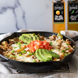 Skillet with breakfast dish topped with avocado and tomatoes, with Olvelle products in the background.