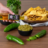 Olive oil bottle being poured over chips with guacamole and peppers on a wooden surface