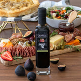 Bottle of Olivelle Harvest Fig balsamic vinegar on a wooden table with a charcuterie board in the background.