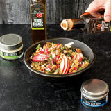 Person pouring olive oil over a salad with various seasonings on a dark surface